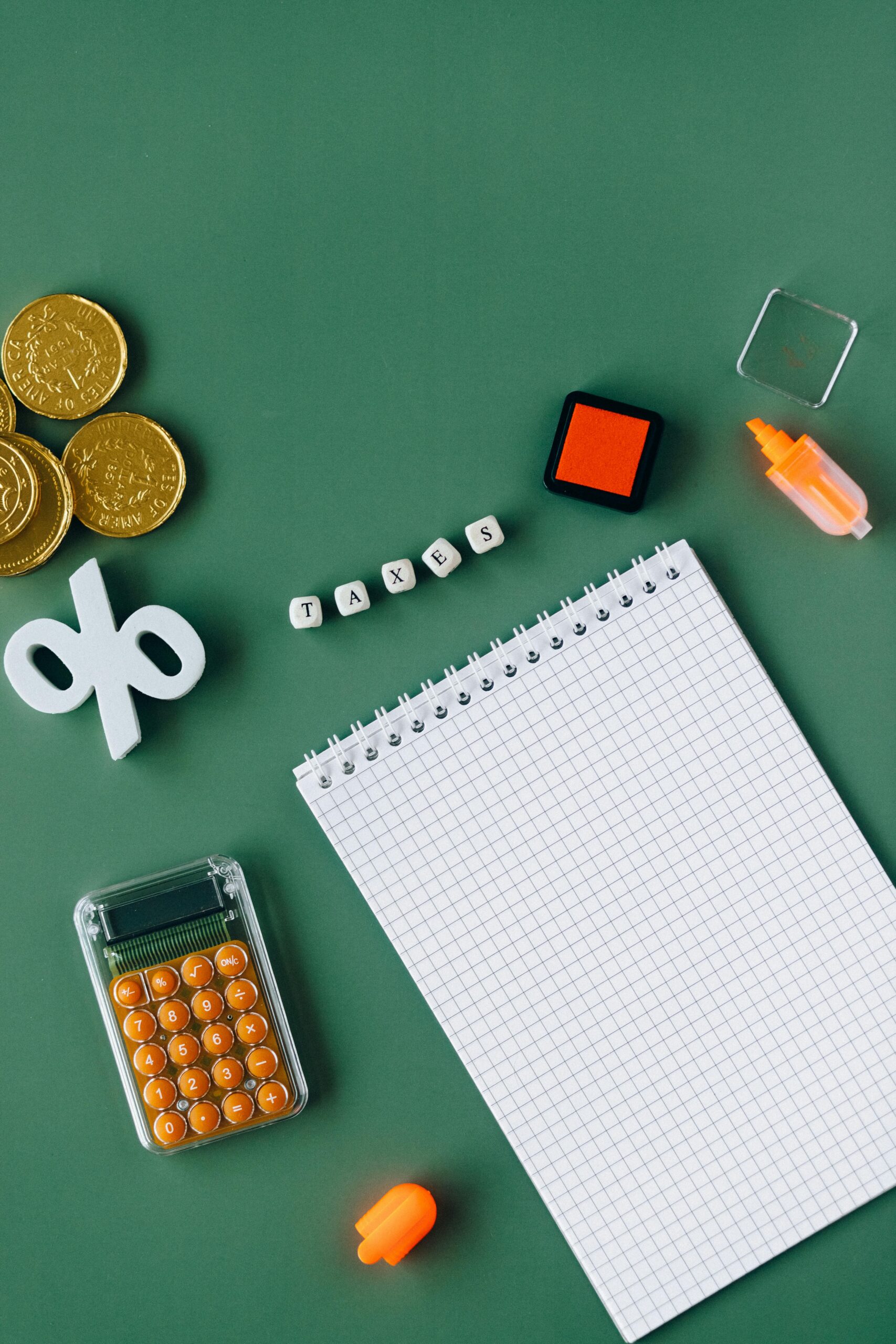 Calculator, coins, notepad and tax-related items arranged on a green background to illustrate tax and inheritance tax planning.